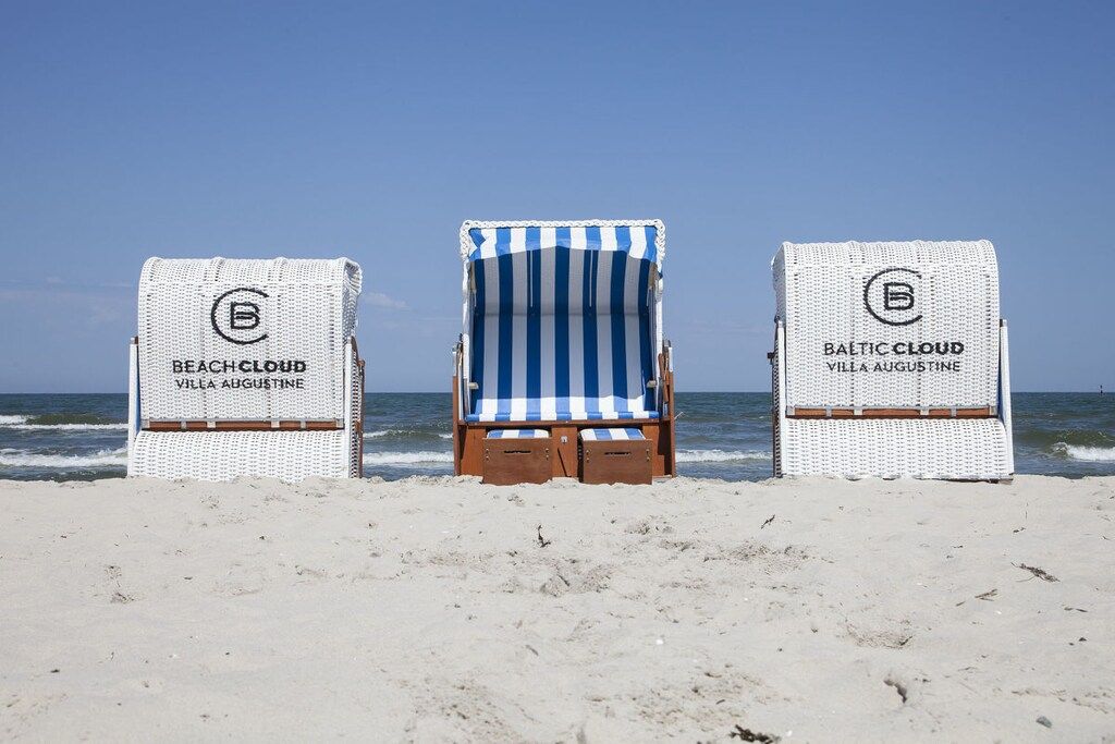 Trois chaises de plage portant la marque « Beach Cloud Villa Augustine », disposées sur une plage de sable, avec l’océan en arrière-plan.