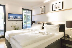 A modern hotel room with a large bed, a television mounted on the wall, and a window with a view of greenery. - Baltic Cloud at Villa Augustine (Ostseebad Binz)