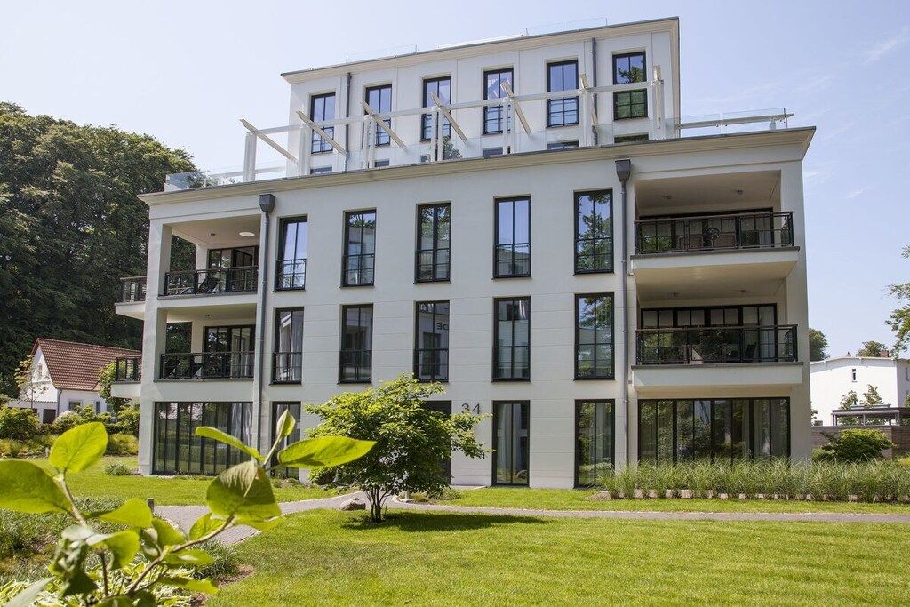 A multi-story building with balconies, large windows, and a well-maintained lawn.
