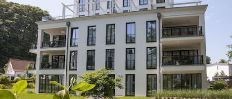 A multi-story building with balconies, large windows, and a well-maintained lawn.