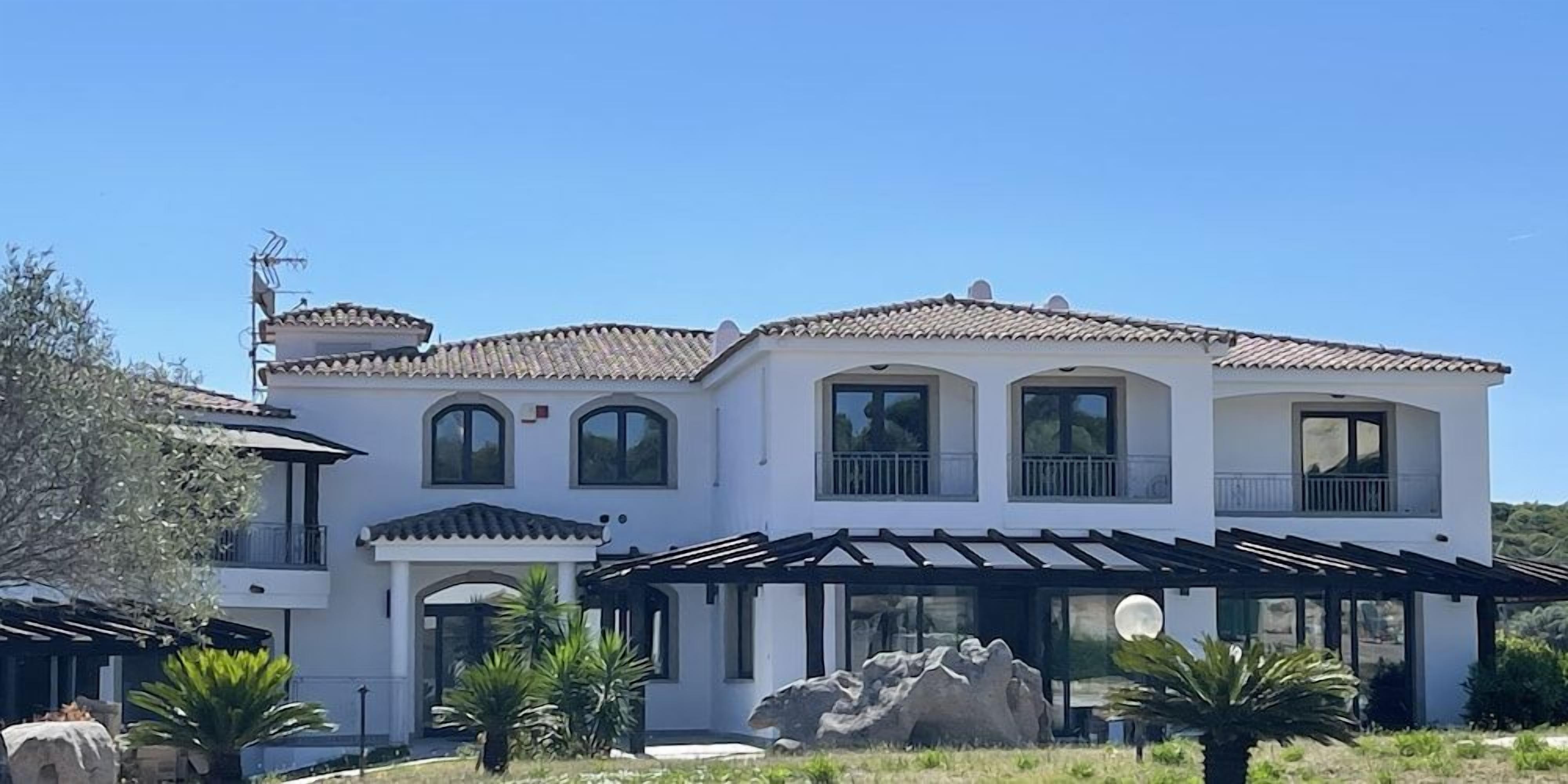 A two-story house with a tiled roof, multiple windows, and a covered patio area.
