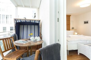 A hotel room with a bed, a small table with a chair, a window with curtains, and a view of buildings outside. - 6 (Seagull) in Villa Helene (Ostseebad Binz)
