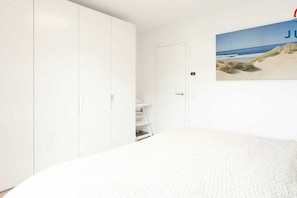 Ein Schlafzimmer mit Bett, Schrank, einer Tür und Wandbildern zum Thema Strand.