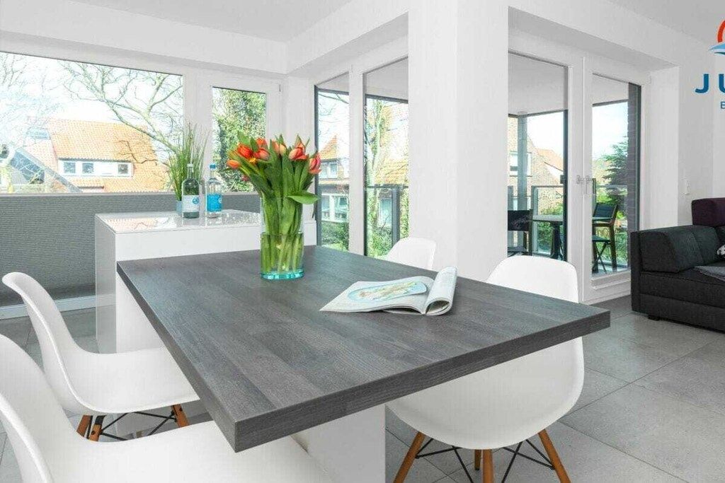 A modern dining area with a dark wood table, white chairs, and a vase of flowers.