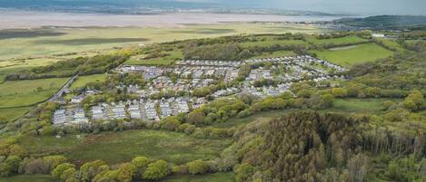 Vista aérea de una zona residencial con casas dispuestas en un patrón semicircular, rodeada de campos verdes y un área boscosa.