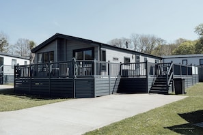 A modern mobile home with a fenced deck and a staircase leading to the entrance.