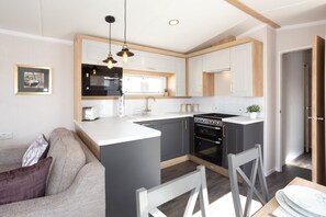 A modern kitchen with a central island, built-in appliances, and pendant lighting. - Llanrhidian Holiday Park (Swansea)