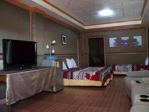 Una habitación de hotel con televisión, un escritorio con lámpara, una cama con colcha estampada y un sofá.