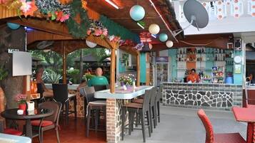 An outdoor café with tables and chairs, a stone wall, and a bar area with bottles.