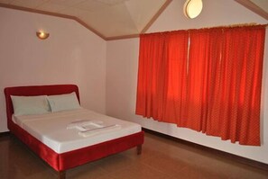 Una habitación con una cama, una ventana con cortinas rojas y una lámpara en el techo.