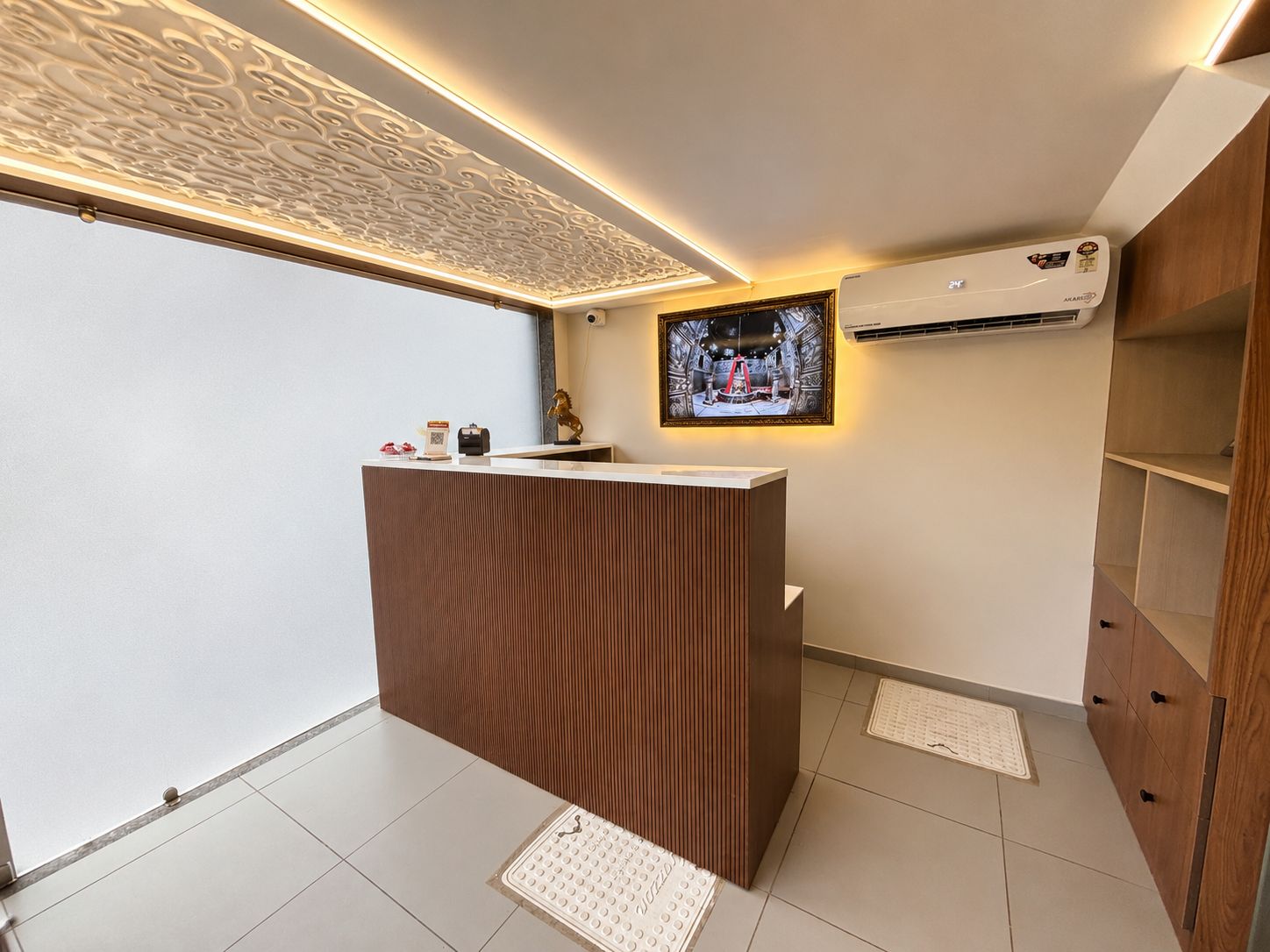 Un área de recepción con un mostrador de madera, un televisor montado y una unidad de aire acondicionado en la pared.