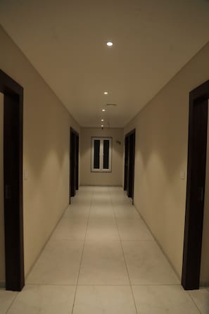 A long, narrow hallway with doors on both sides, leading to a room with a large window. - Hotel Lakshmi Tara (Ujjain)