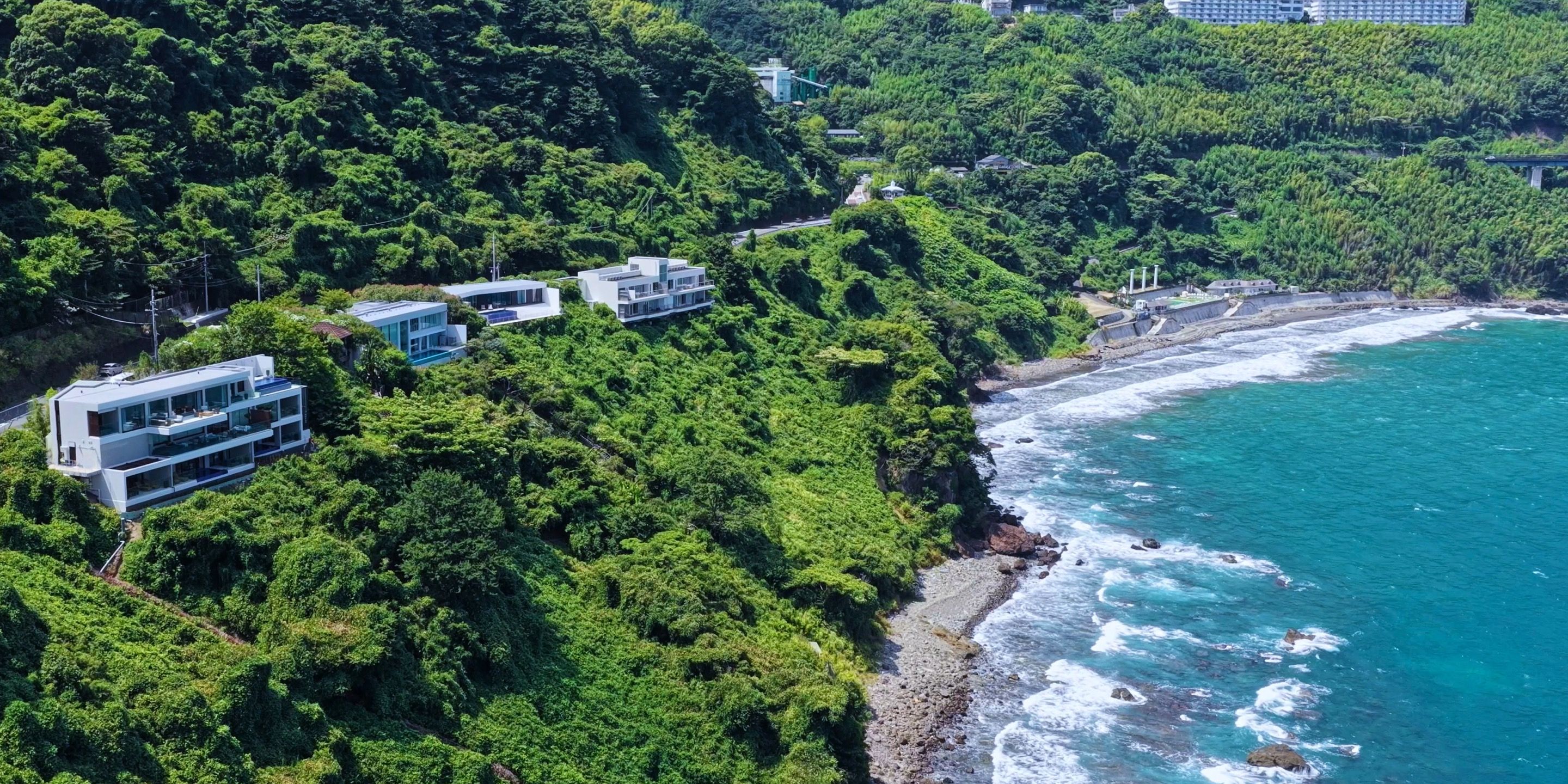 Una propiedad costera con edificios modernos integrados en abundante vegetación, con vistas a un litoral rocoso.