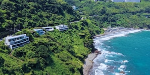 A coastal property with modern buildings nestled among dense greenery, overlooking a rocky shoreline. - UMITO ATAMI THE SALON (Atami)