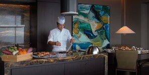 Un chef preparando comida en una cocina moderna con encimera de mármol y un cuadro abstracto grande en la pared.