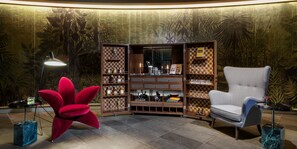Una habitación de esquina con una estantería a cuadros, un sillón floral rojo, un sillón gris y una lámpara de pie.
