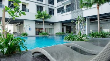 A modern indoor pool area with a lounge chair, surrounded by potted plants and a multi-story building with balconies.