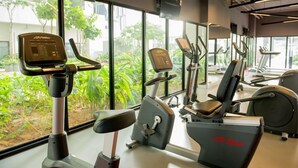 A gym with cardio machines, weight machines, and a large window with a view of greenery. - Ezzyhome @ Medini (Iskandar Puteri)