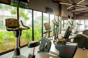 A gym with cardio machines, weight machines, and a large window with a view of greenery. - Ezzyhome @ Medini (Iskandar Puteri)