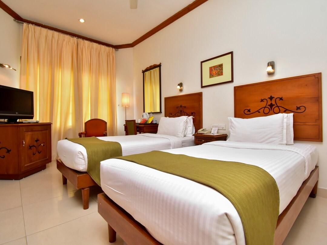 A hotel room with two beds, a TV, a desk, and a window with curtains.