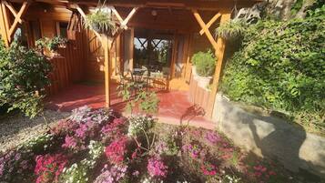 Een houten constructie met een overdekt terras, een tuin met diverse planten en een zitgedeelte met een tafel en stoelen.
