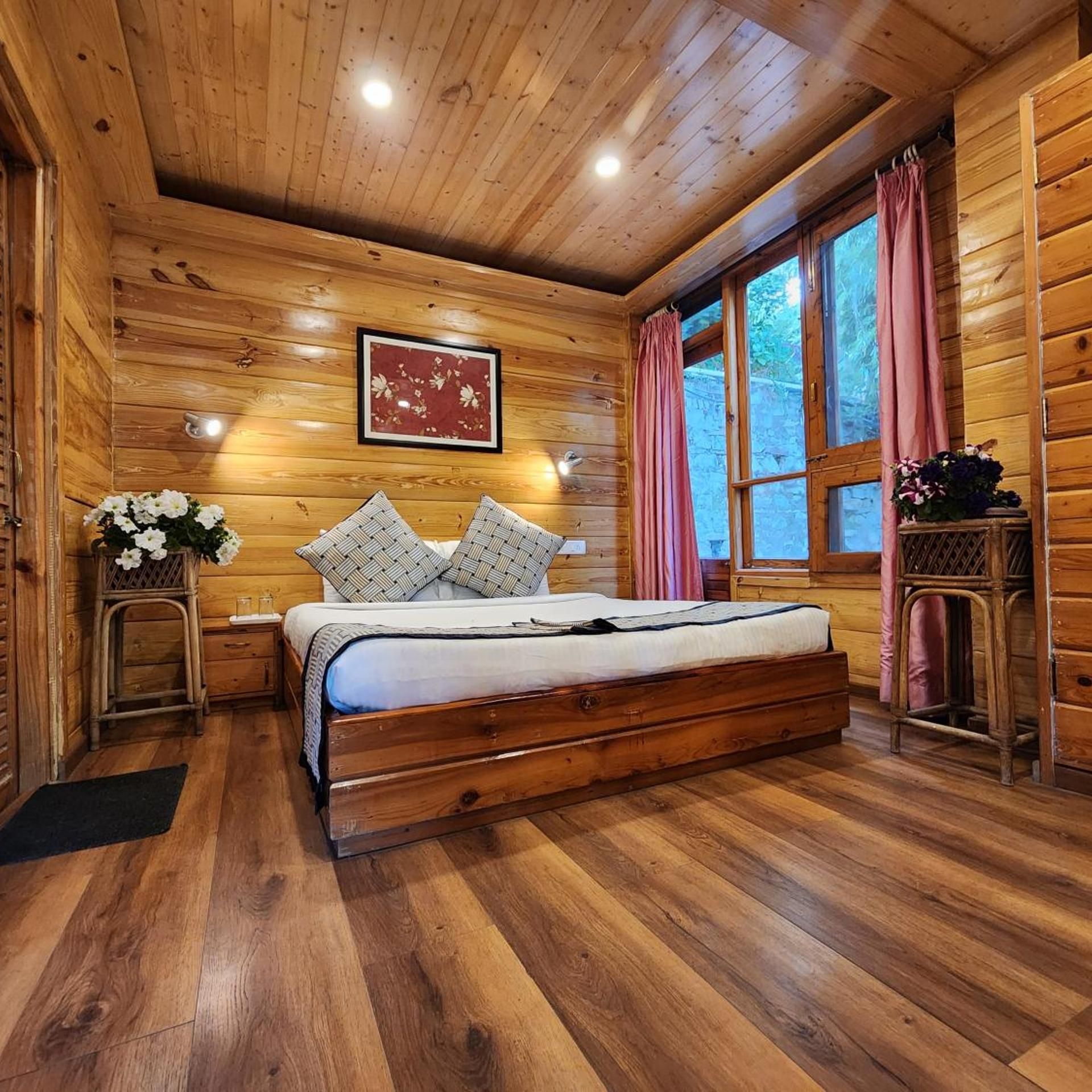 Een slaapkamer in een houten chalet met een bed, een nachtkastje, een raam met gordijnen en een ingelijste foto aan de muur.