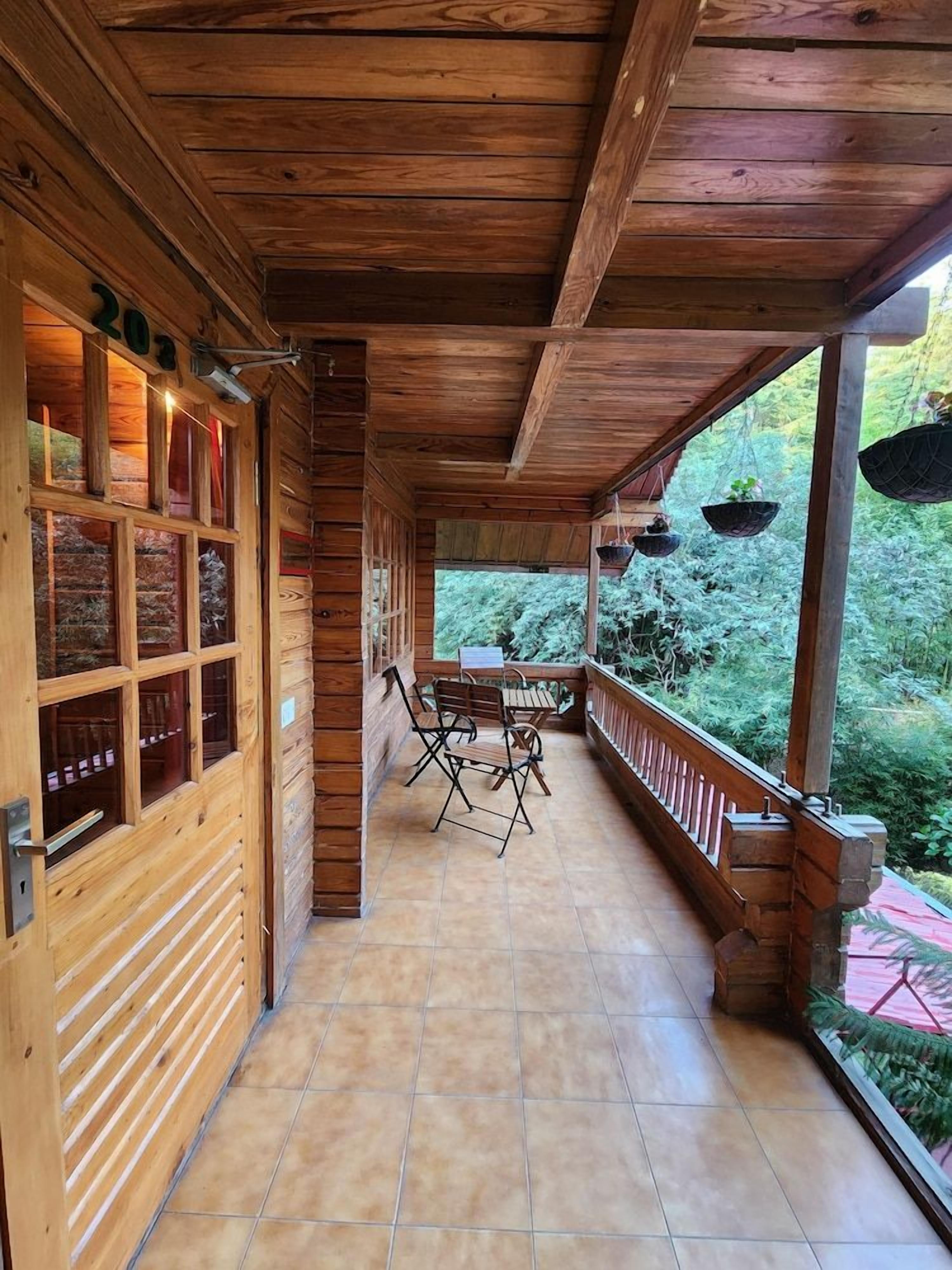 Een houten veranda met tegels, een tafel, stoelen en uitzicht op groen.