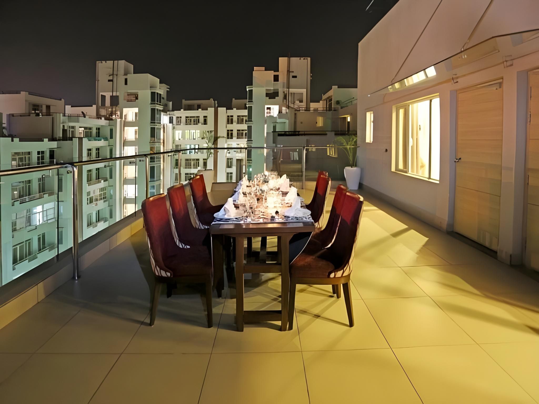 Een eetgedeelte met een tafel en stoelen op een terras op het dak, met uitzicht op een stadsgezicht in de nacht.