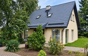 A two-story house with a sloped roof, a chimney, and a garden with various plants and flowers.