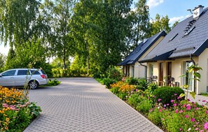 A paved driveway leading to a building with a sloped roof, surrounded by lush greenery and flowering plants.