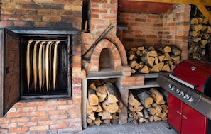A brick oven with a window, a grill, and stacked firewood.
