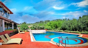 Una piscina con sillas de descanso y un área junto a la piscina, rodeada de follaje.
