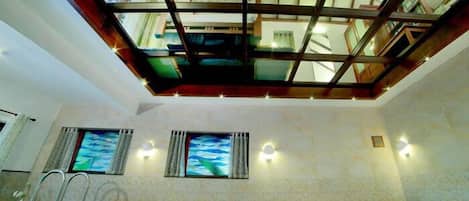 A room with a skylight, two windows with curtains, a pool, and a ladder.