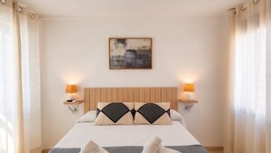 Una habitació d'hotel amb un llit, dues làmpades de nit, un quadre a la paret i una finestra amb cortines.