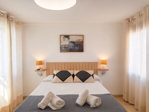 Ein Hotelzimmer mit einem Bett, zwei Nachttischlampen, einem Bild an der Wand und einem Fenster mit Vorhängen.