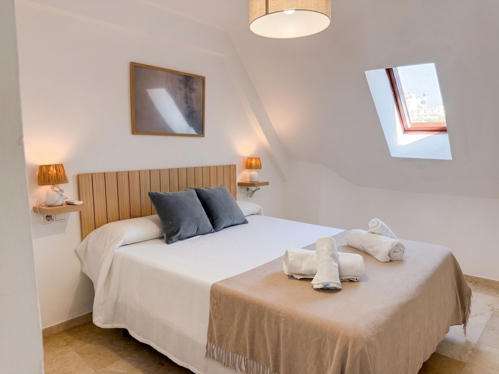 Une chambre à coucher avec un lit, des oreillers, une lampe de chevet, une fenêtre et une serviette sur le lit.