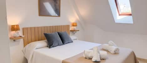 Une chambre à coucher avec un lit, des oreillers, une lampe de chevet, une fenêtre et une serviette sur le lit.