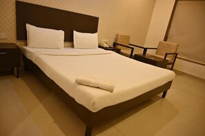 Una cama bien hecha con sábanas blancas, cabecera de madera y dos sillas de estructura de madera.