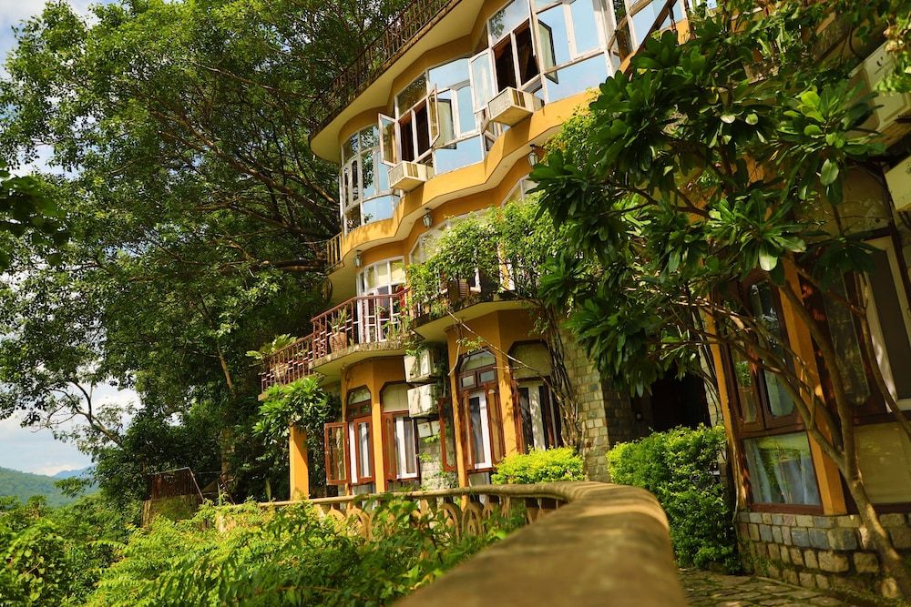 A multi-story building with balconies, surrounded by lush greenery.