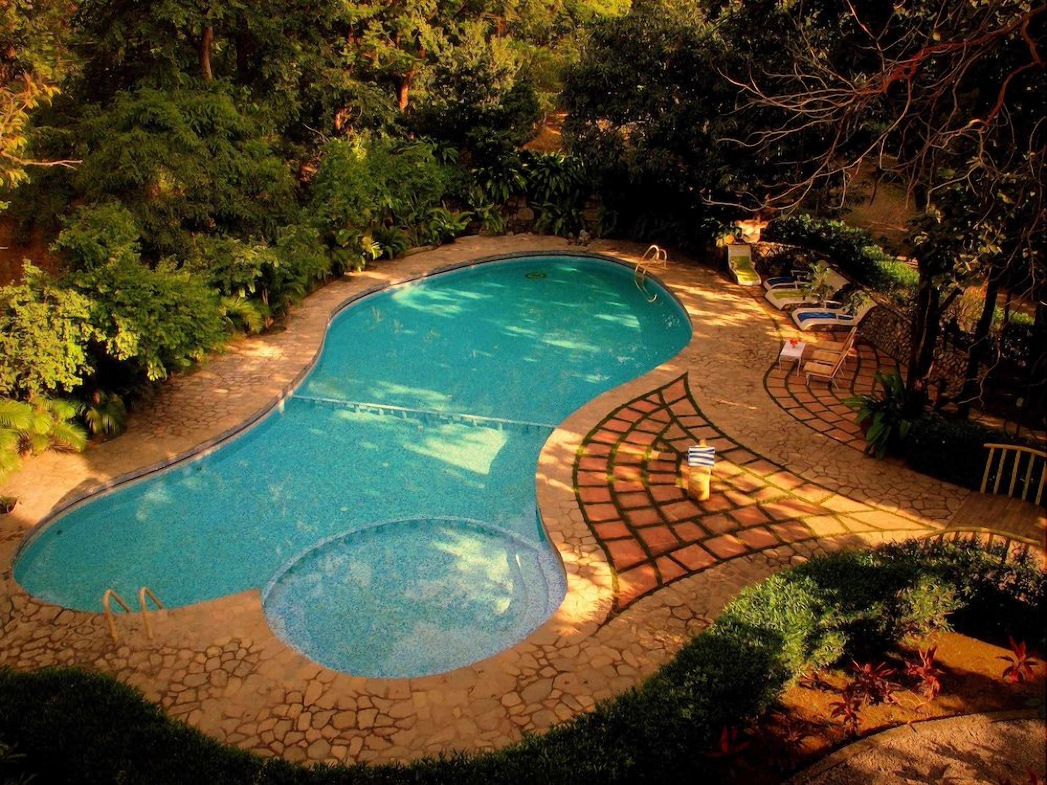 A swimming pool with a curved design, surrounded by a stone pathway and lush greenery.
