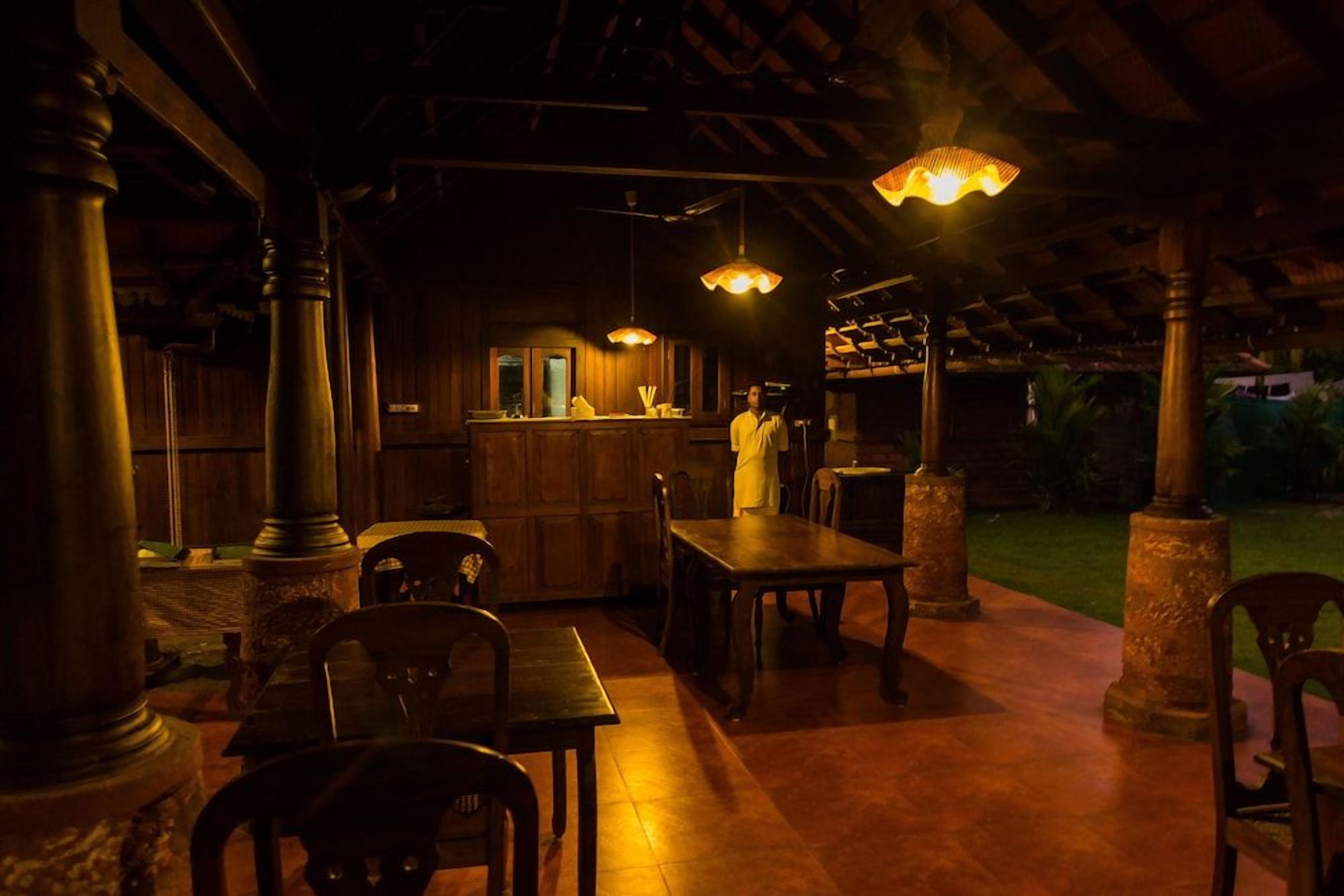 An outdoor dining area with wooden tables and chairs, a bar counter, and hanging pendant lights.