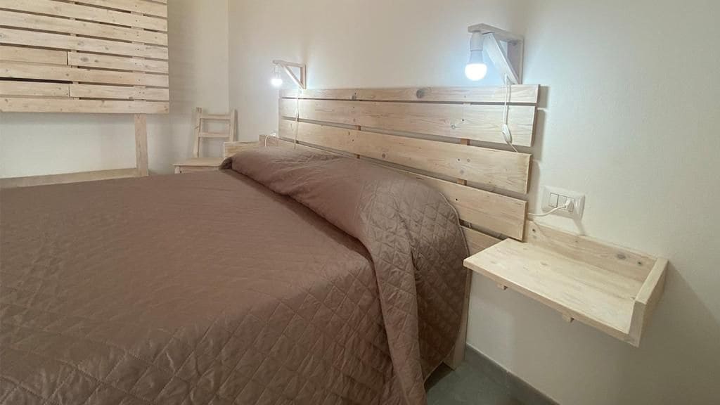 Ein Schlafzimmer mit einem Bett, einem Nachttisch, einem Wandregal und einem Sessel.
