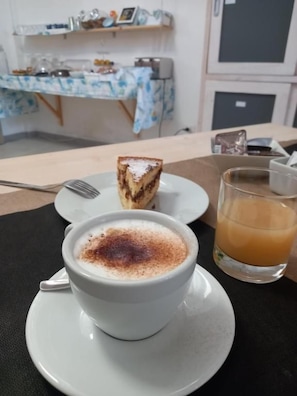 A cup of coffee with a slice of cake on a plate, a glass of orange juice, and a fork on a table.
