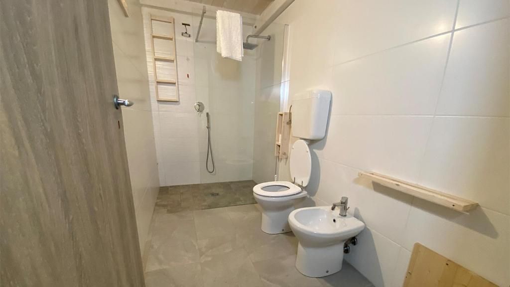 A bathroom with a shower, two toilets, a bidet, and a soap dispenser.