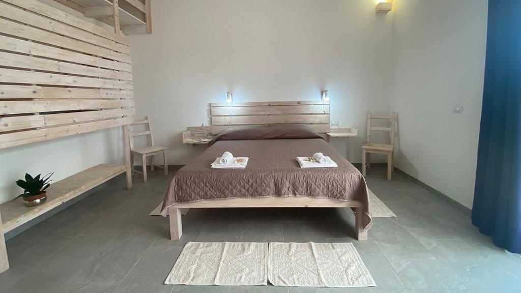 Ein Schlafzimmer mit einem hölzernen Bett, zwei Nachttischen, einer Stehlampe und einem Blumentopf, dazu ein blauer Vorhang.
