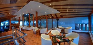 A modern interior with a bar area, seating, and large windows offering views. - Chail Villas (Shimla)