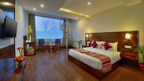 Habitación de hotel con una cama grande, televisión, escritorio, silla, escalera y ventana con cortinas.