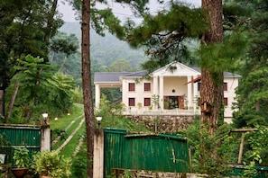 A two-story building with a white facade and a balcony, surrounded by lush greenery and trees. - Royal Heritage-tripura Castle (Shillong)