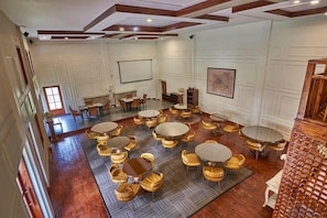 A spacious room with multiple round tables and chairs, wooden flooring, and a high ceiling with exposed beams. - Royal Heritage-tripura Castle (Shillong)