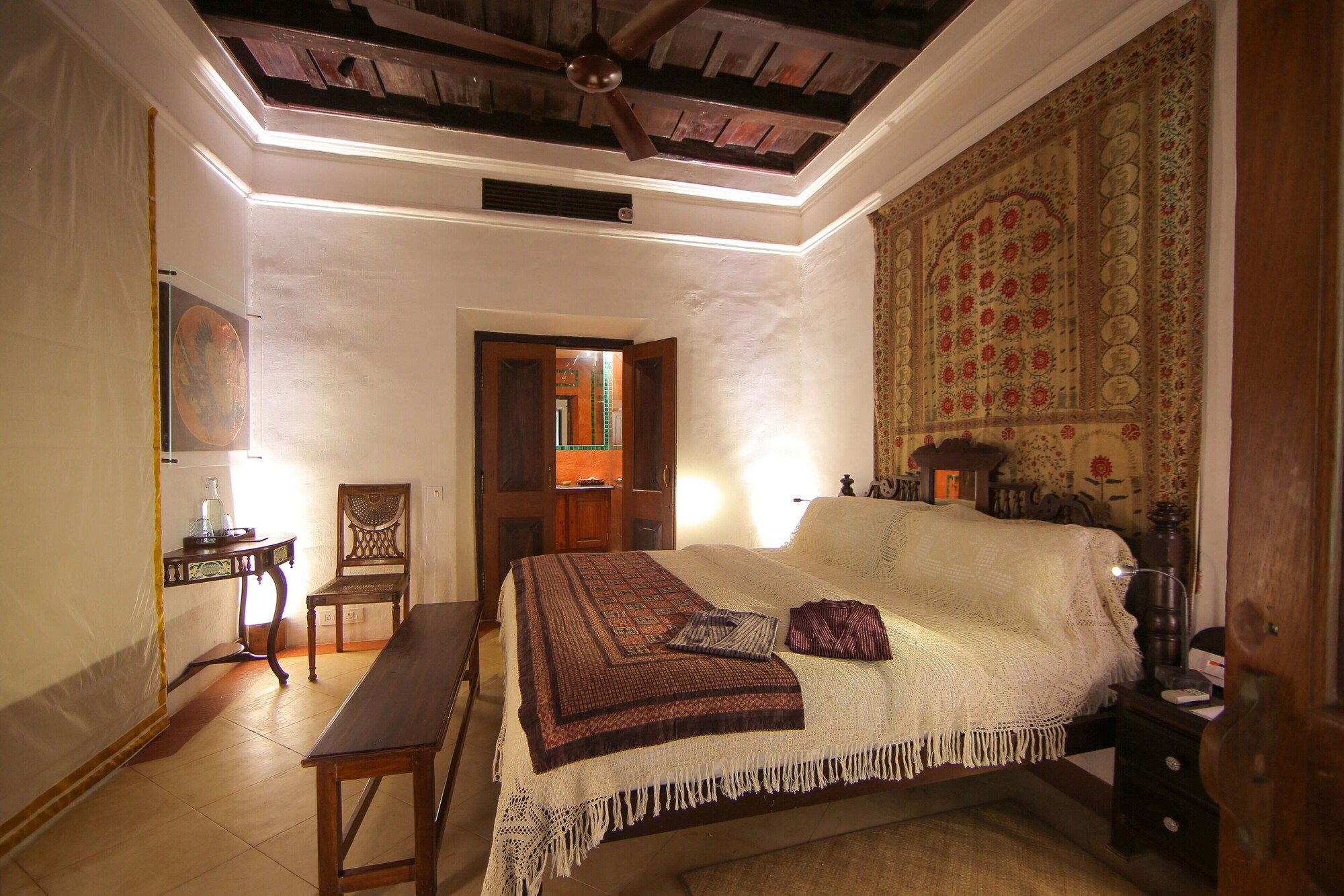 A bedroom with a large bed, a wooden bench, a chair, and a tapestry on the wall.
